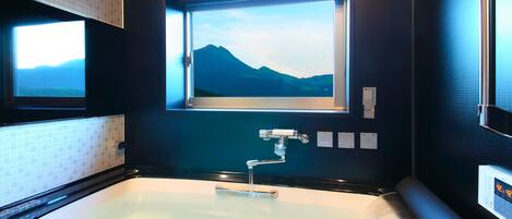 A modern bathroom with a large bathtub, a window with a mountain view, and a control panel on the wall.