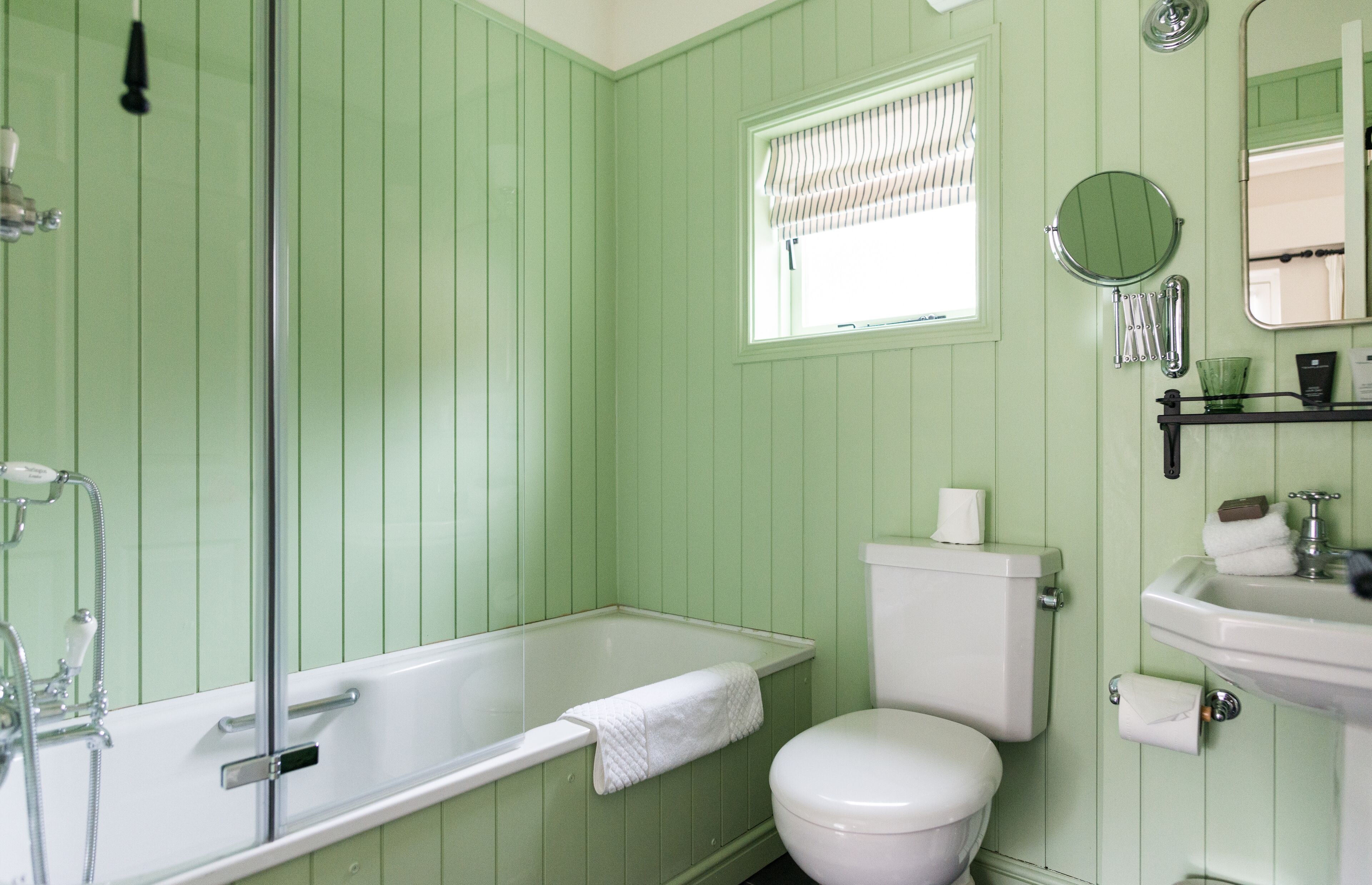 Een badkamer met bad, toilet, wastafel en een raam met zonwering.