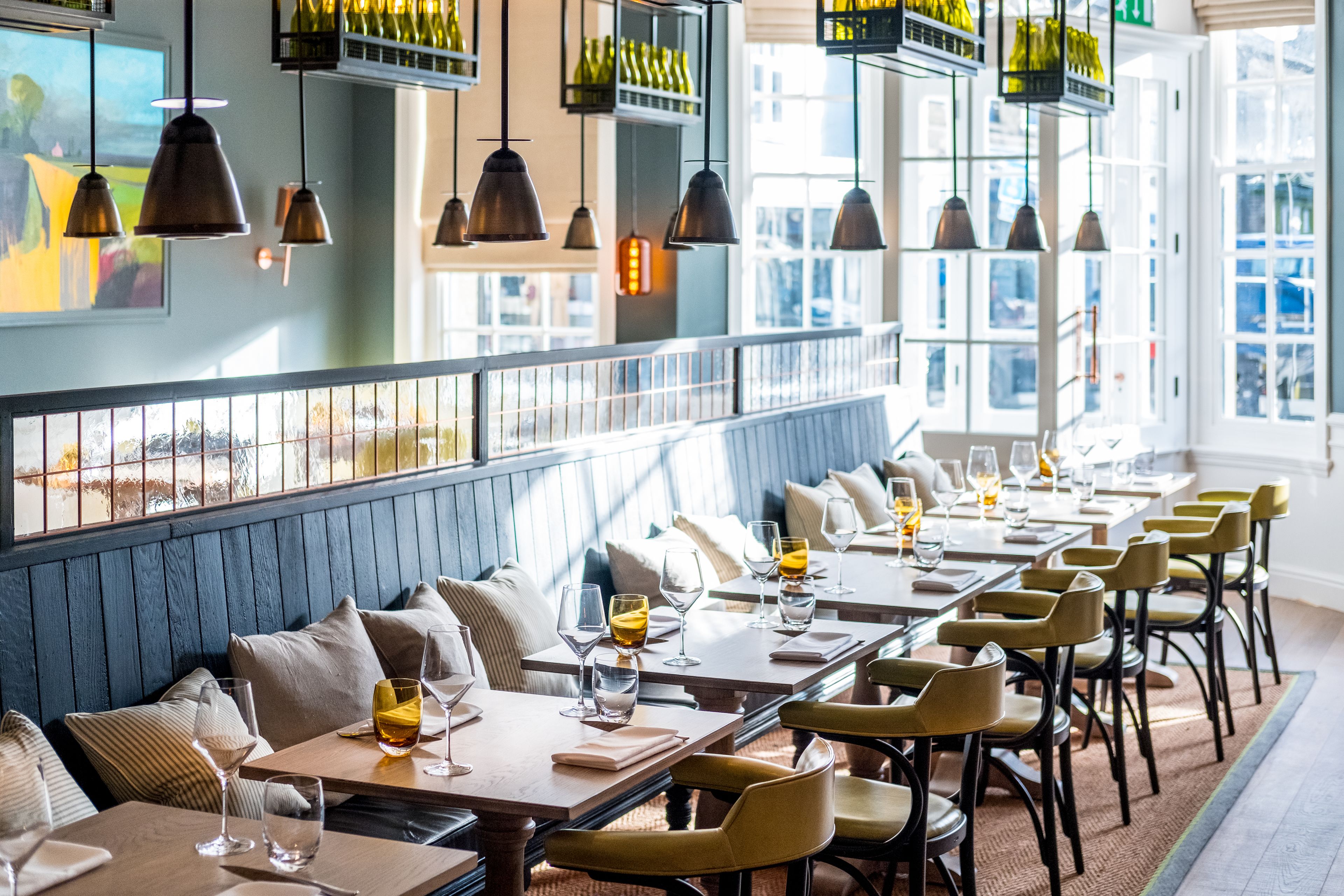A restaurant with long tables, chairs, and hanging pendant lights.