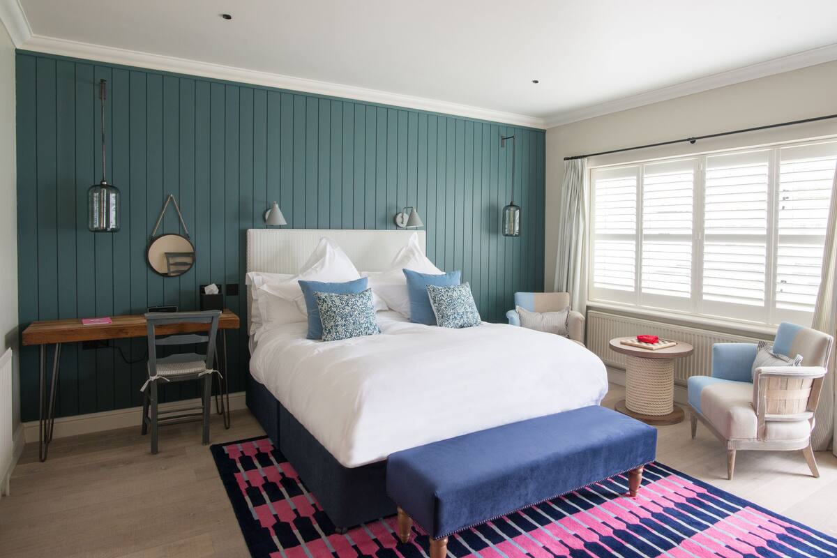 A bedroom with a large bed, a desk, a chair, and a window with curtains.