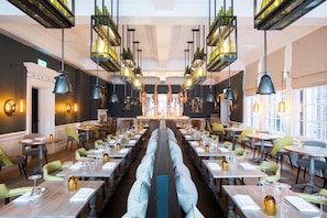 Un restaurant avec une allée centrale, des tables, des chaises, des luminaires suspendus et une vue sur la rue.