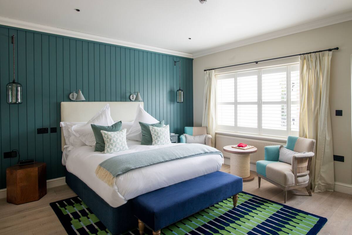 A bedroom with a large bed, a bedside table, a chair, a window with curtains, and a small round table.