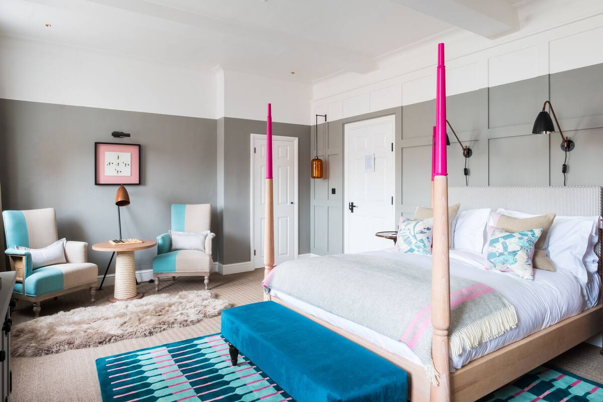 A bedroom with a four-poster bed, two armchairs, a round side table, and a fluffy rug.
