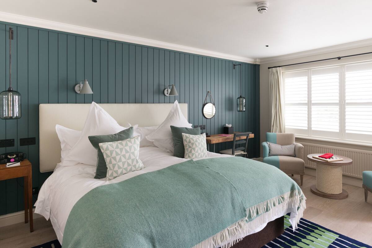 A bedroom with a large bed, a desk, a chair, and a window with blinds.