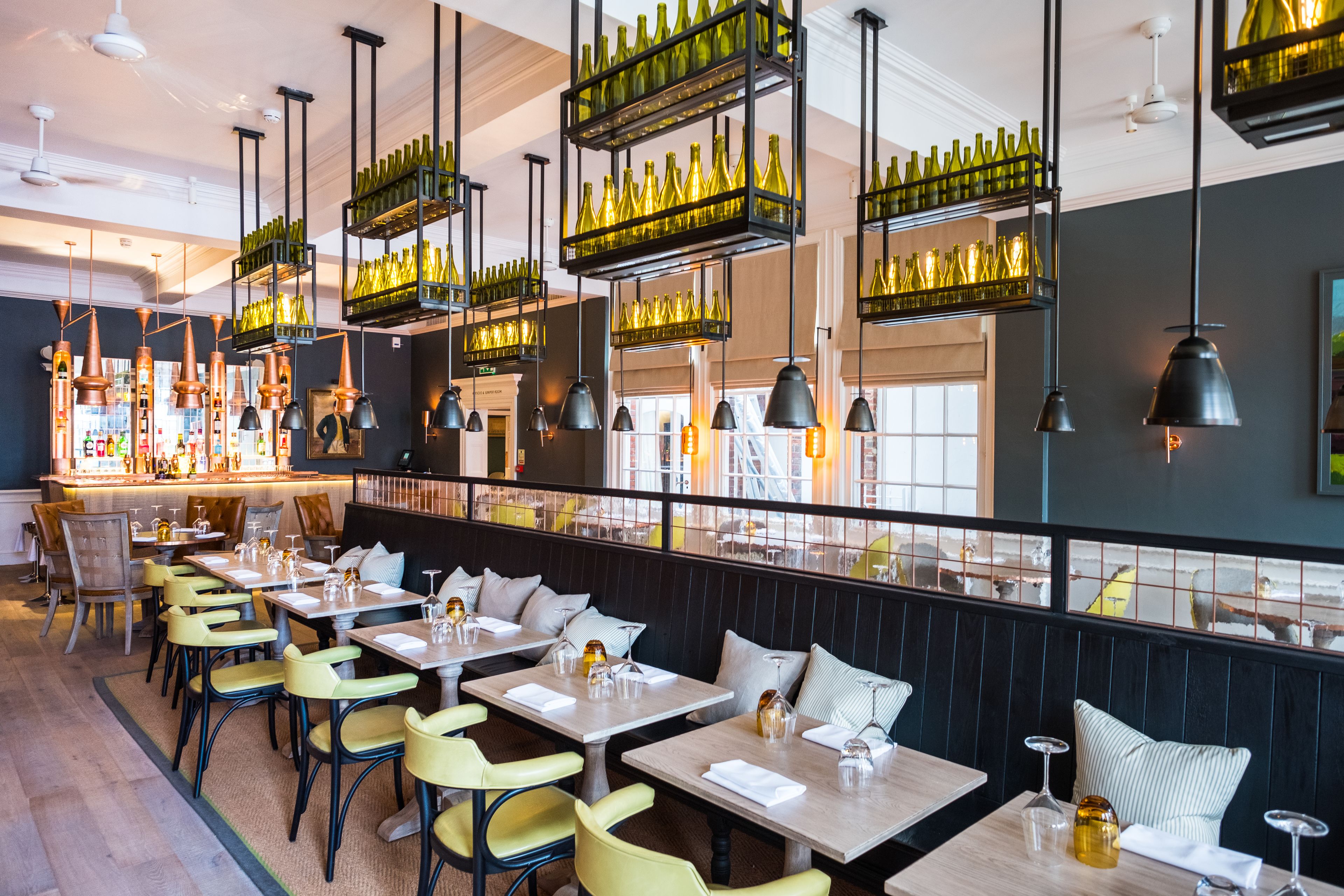 Interior de restaurante con varias mesas, sillas, estanterías con botellas de vino y una zona de bar.