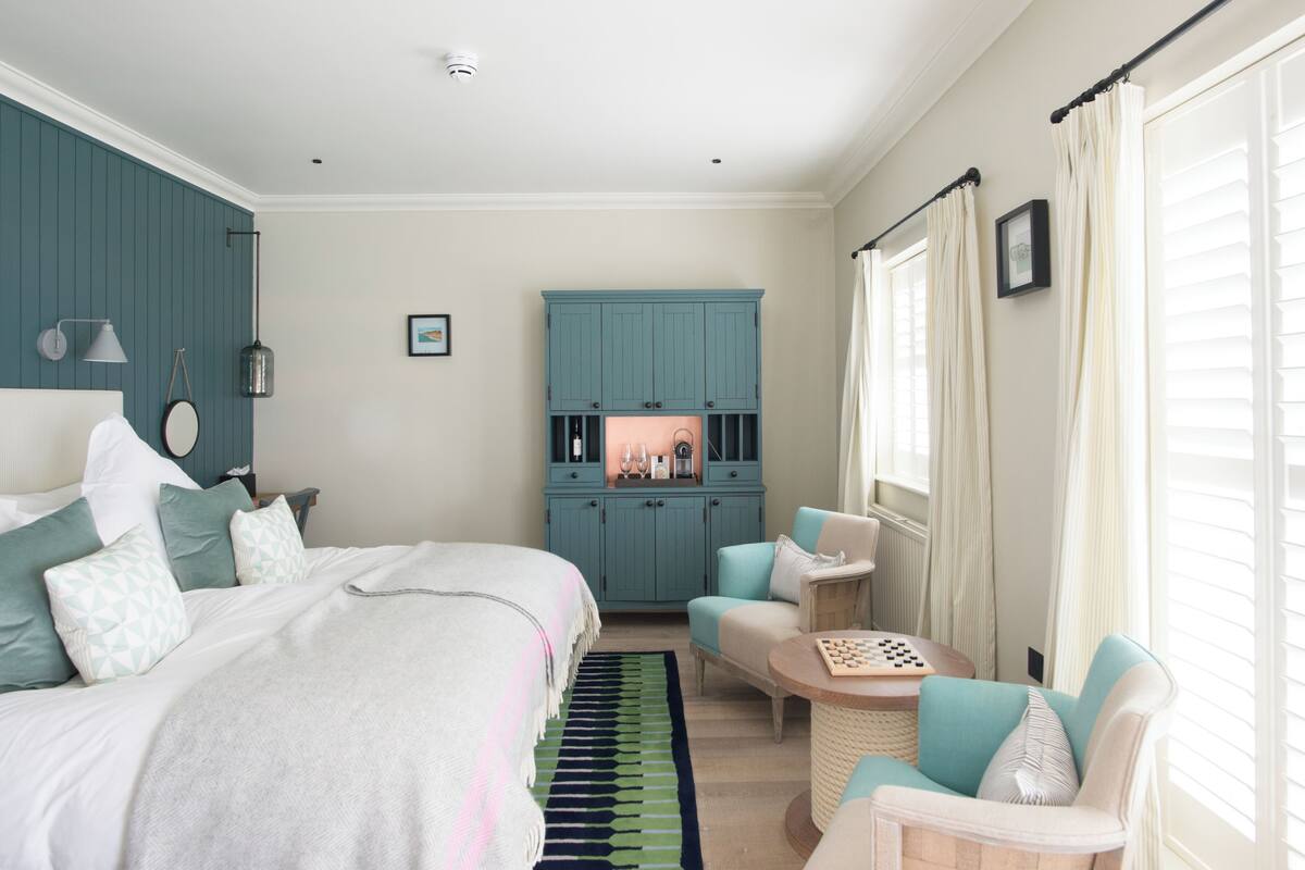 A bedroom with a bed, a seating area with a table, and a cabinet with a mirror.