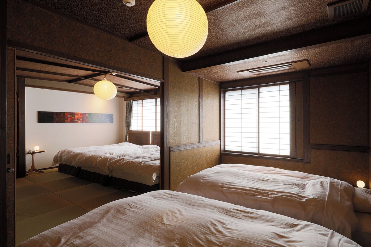 A traditional Japanese-style room with tatami flooring, two beds, a shoji screen window, and a hanging paper lantern.