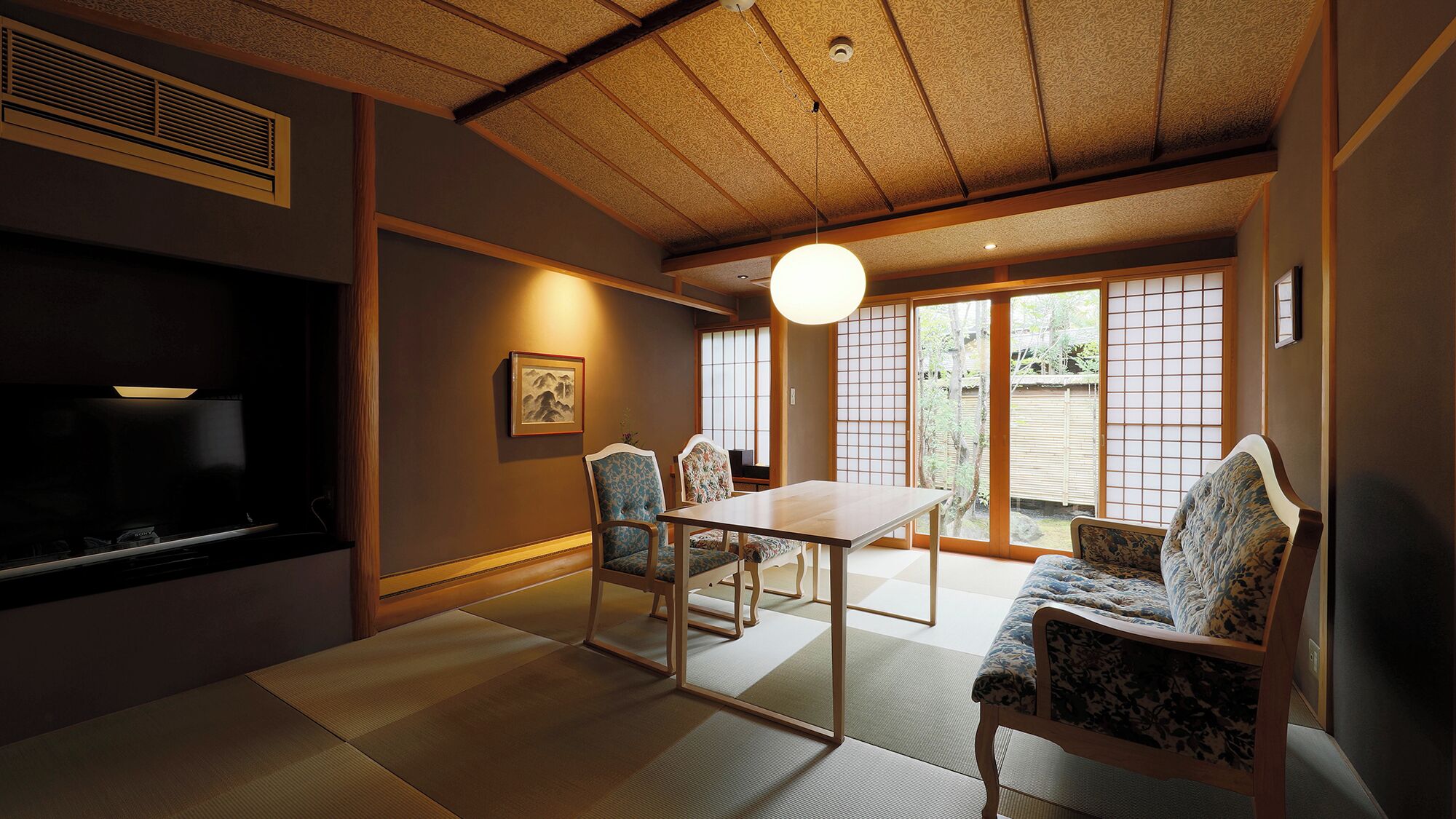 A traditional Japanese room with tatami flooring, a low table, and chairs.