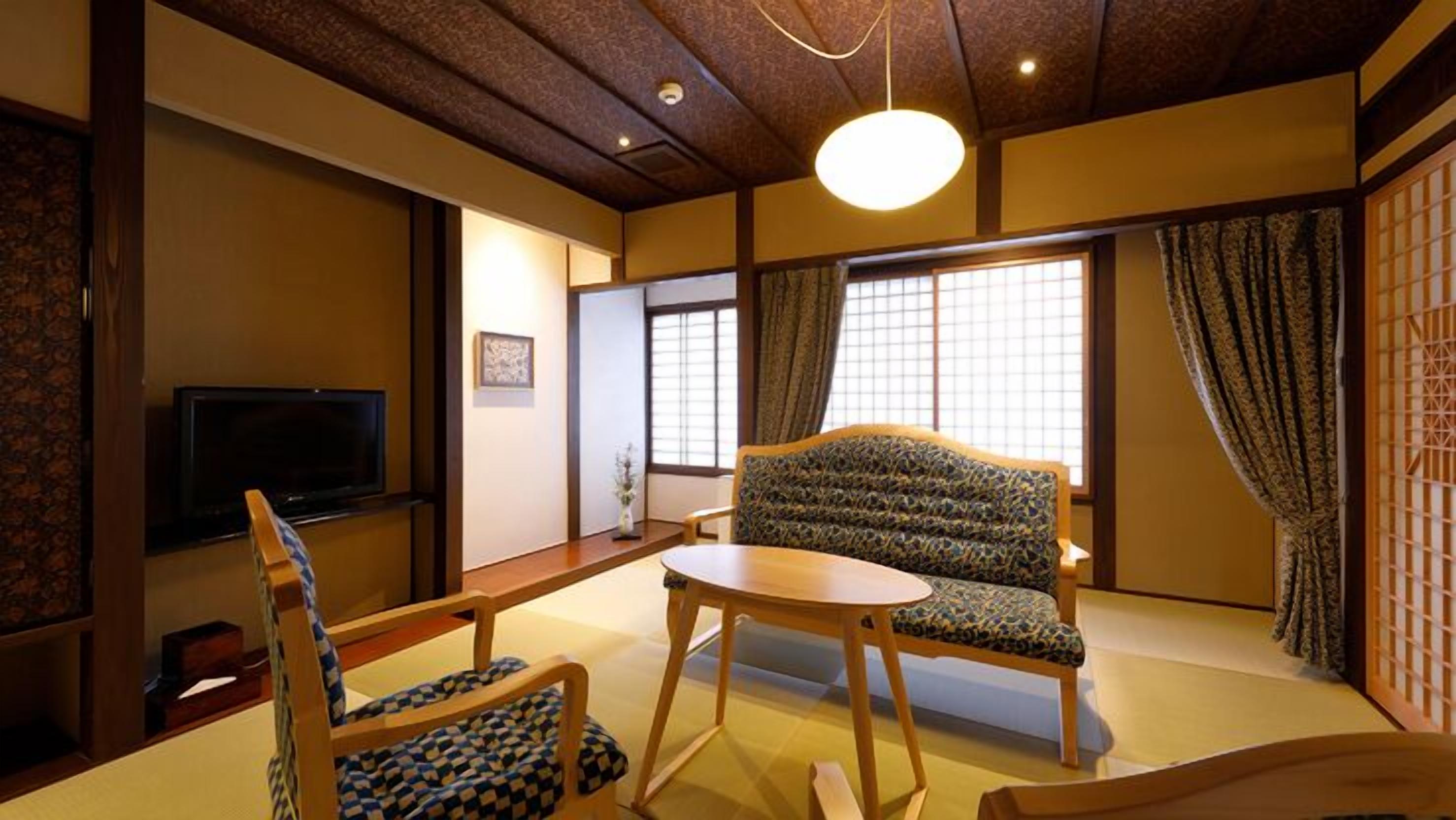 A traditional Japanese room with tatami flooring, a low table, a sofa, and a television.