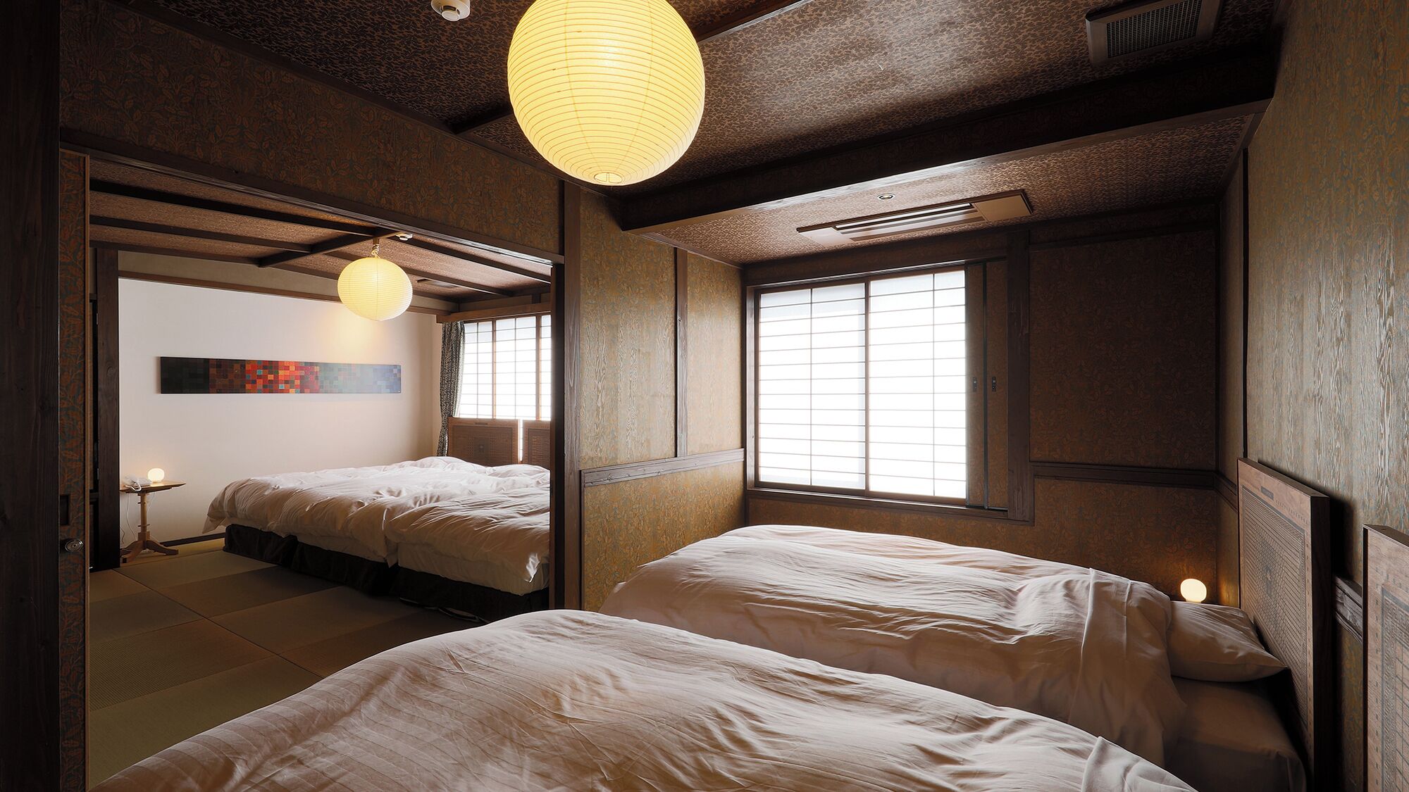 A traditional Japanese-style room with tatami flooring, two beds, a shoji screen window, and a hanging paper lantern.