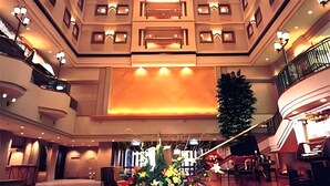 Eine Hotelhalle mit einer großen, zentral platzierten Blumenkomposition, mehreren Ebenen mit Balkonen und einer imposanten Treppe.