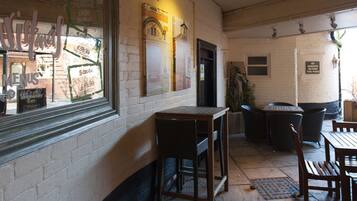 Pared de ladrillo con una ventana que muestra un menú y un cartel. Hay mesas y sillas de madera afuera.