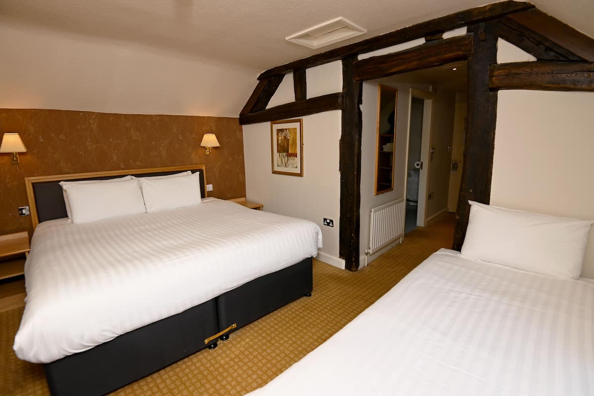 Habitación de hotel con dos camas, vigas de madera, un radiador y una puerta que da a otra habitación.
