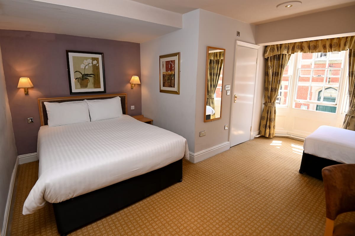 Habitación de hotel con una cama grande, dos lámparas de noche, un espejo y una ventana con cortinas.