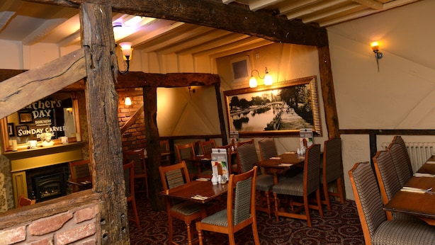 L’intérieur de ce restaurant est chaleureux, avec des poutres en bois, des murs en briques et une cheminée. Les tables et les chaises sont disposées pour accueillir les clients.