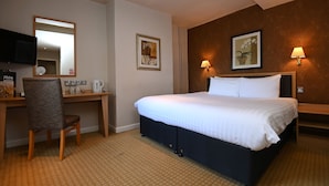Une chambre d’hôtel équipée d’un lit, d’un bureau, d’une chaise et de deux lampes fixées au mur.