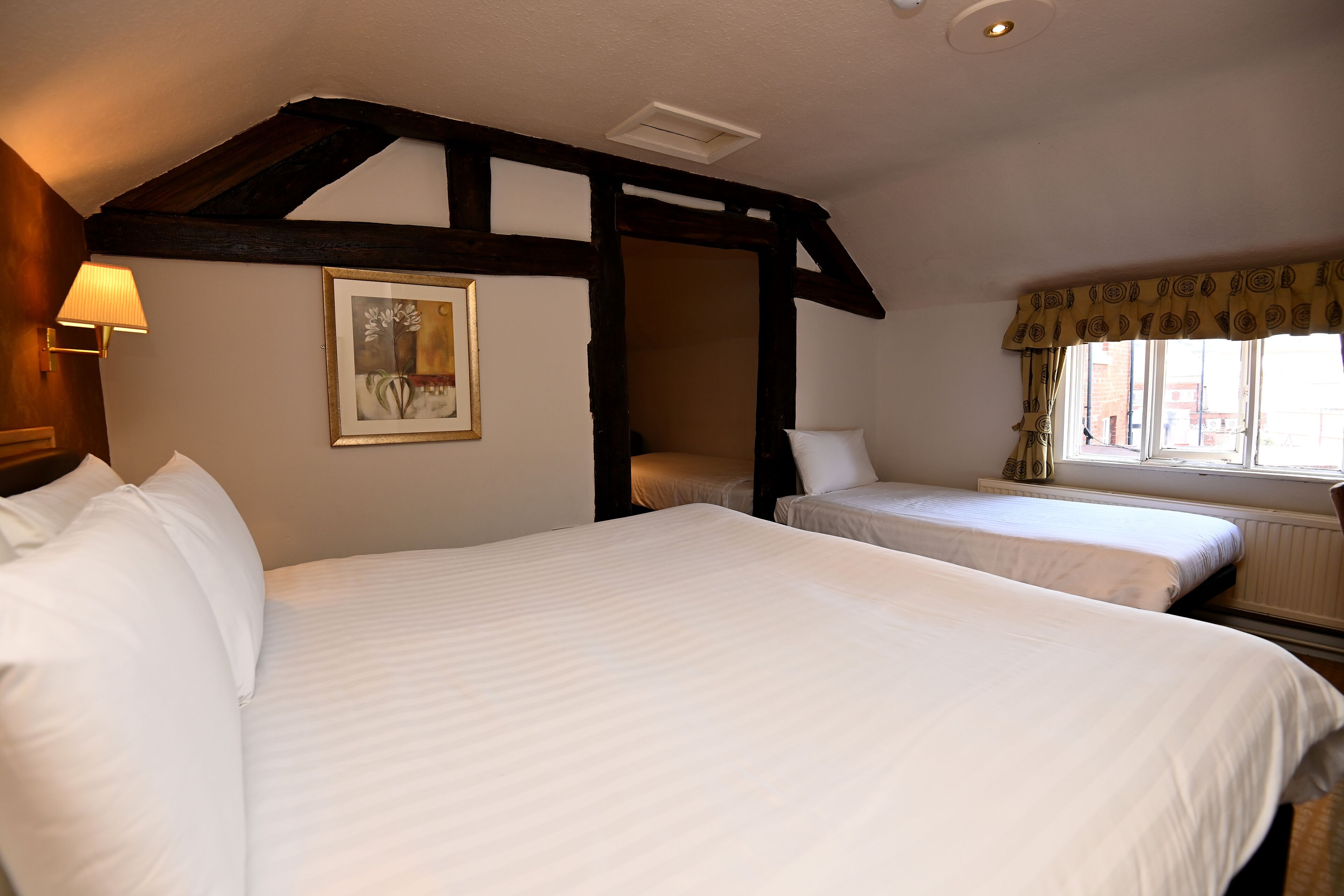 Habitación de hotel con dos camas, techo de madera, ventana con cortinas y un cuadro en la pared.