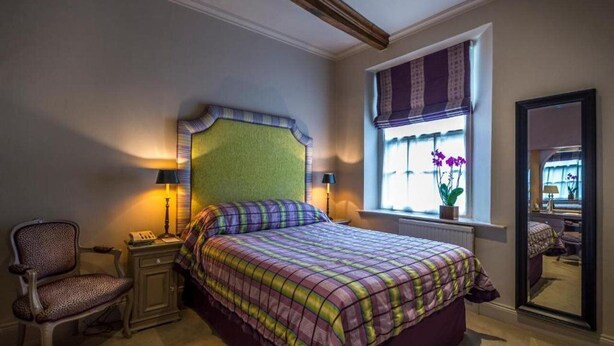A bedroom with a bed, a chair, a nightstand, a window with curtains, and a mirror. - The George Of Stamford (Stamford)