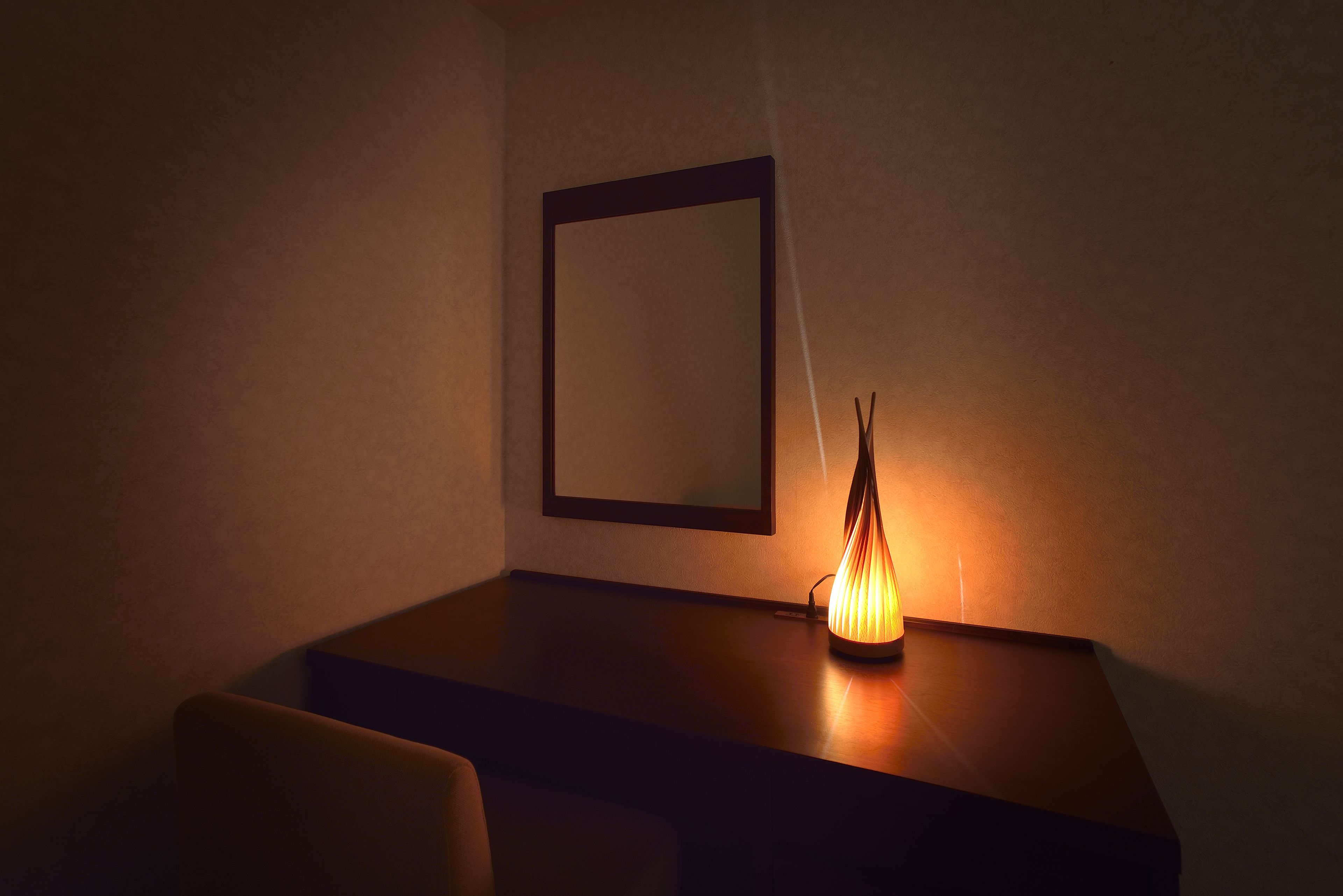 A dark room with a table, a chair, and a lit lamp.