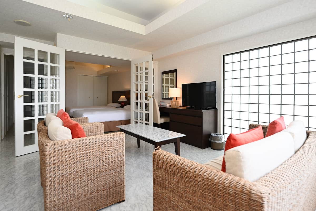 A hotel room with a bed, a TV, wicker furniture, and a large window.