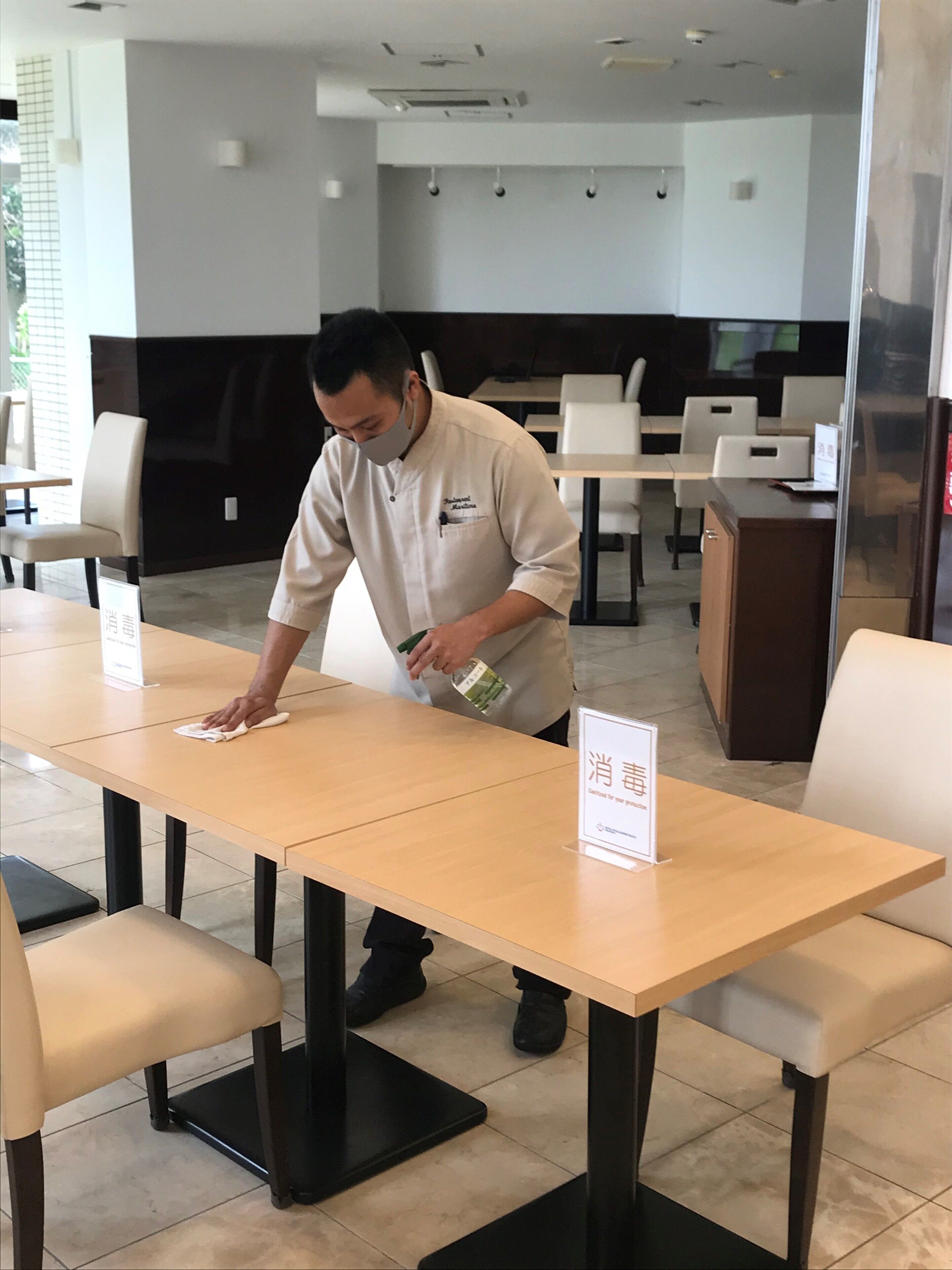 A person cleaning a table in a restaurant with a sign indicating a 4pm closing time.