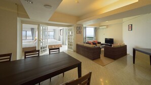 A spacious living area with a dining table, two sofas, a TV, and a balcony with a bed. - Hotel Royal Marine Palace Ishigakijima (Ishigaki)