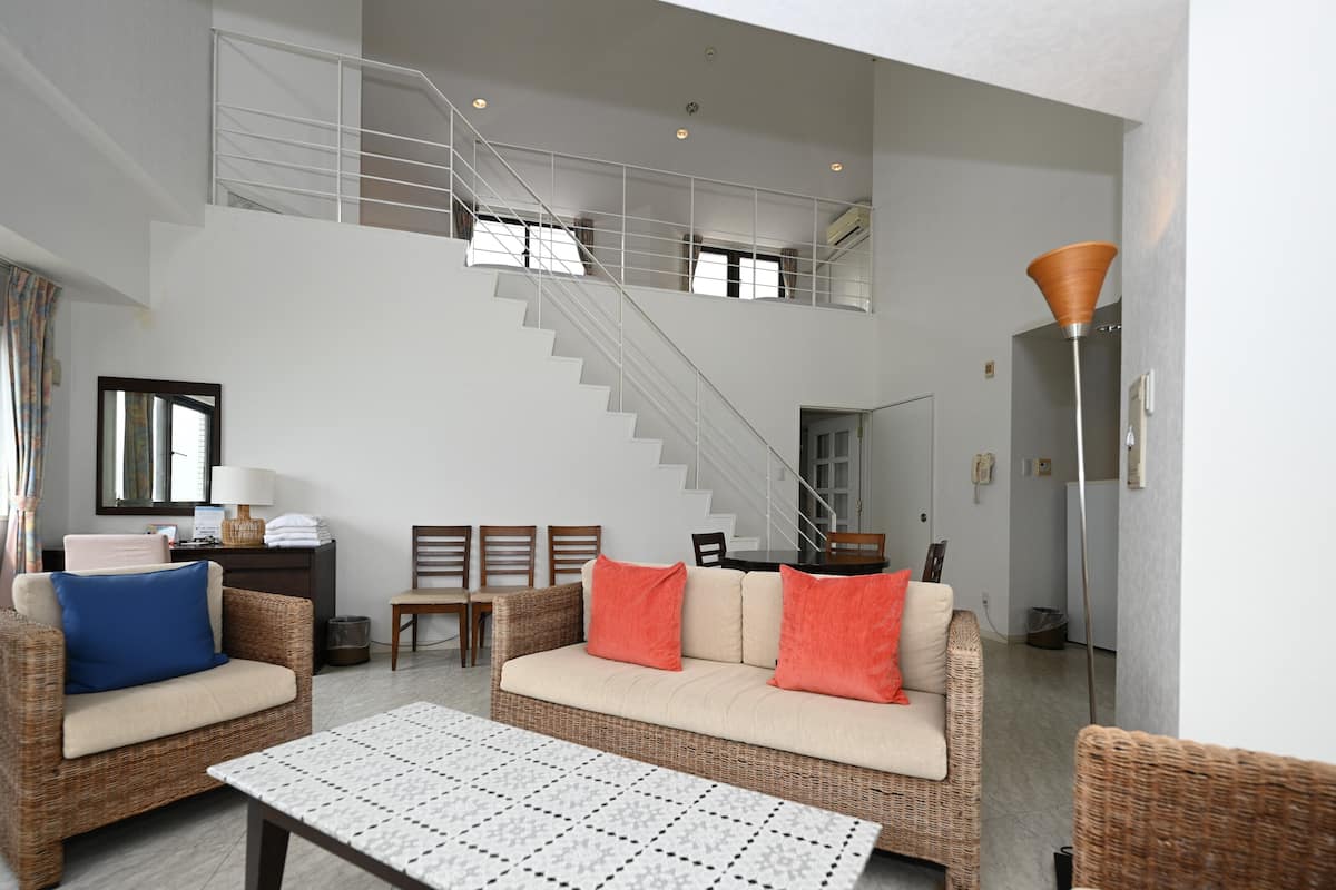 A spacious living area with a high ceiling, a staircase, wicker furniture, and a modern lamp.