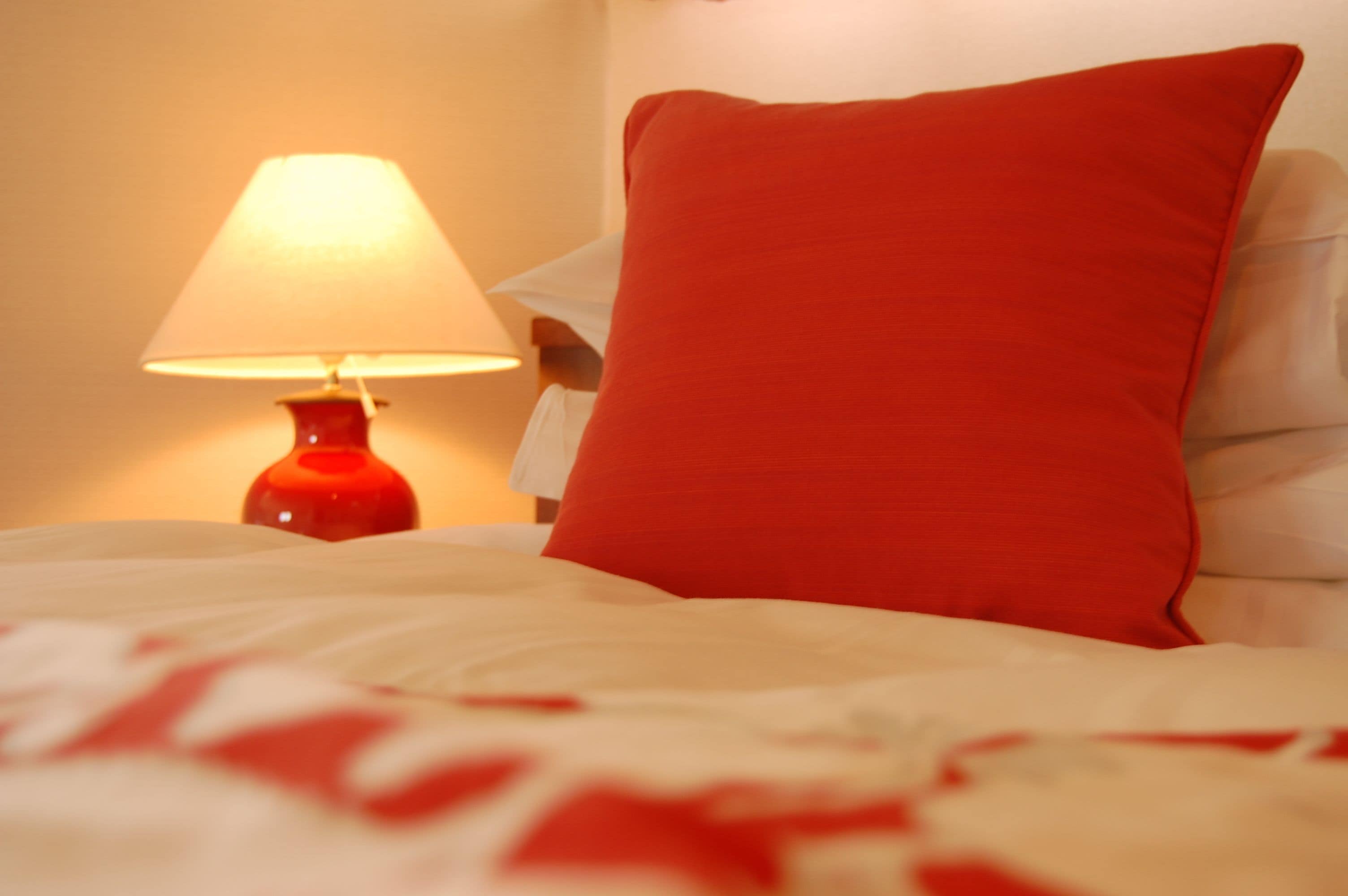 Un lit avec un oreiller rouge et une lampe rouge sur une table de chevet.