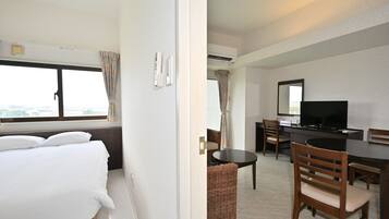 Una habitación de hotel con cama, escritorio, silla, televisor y ventana con cortinas.