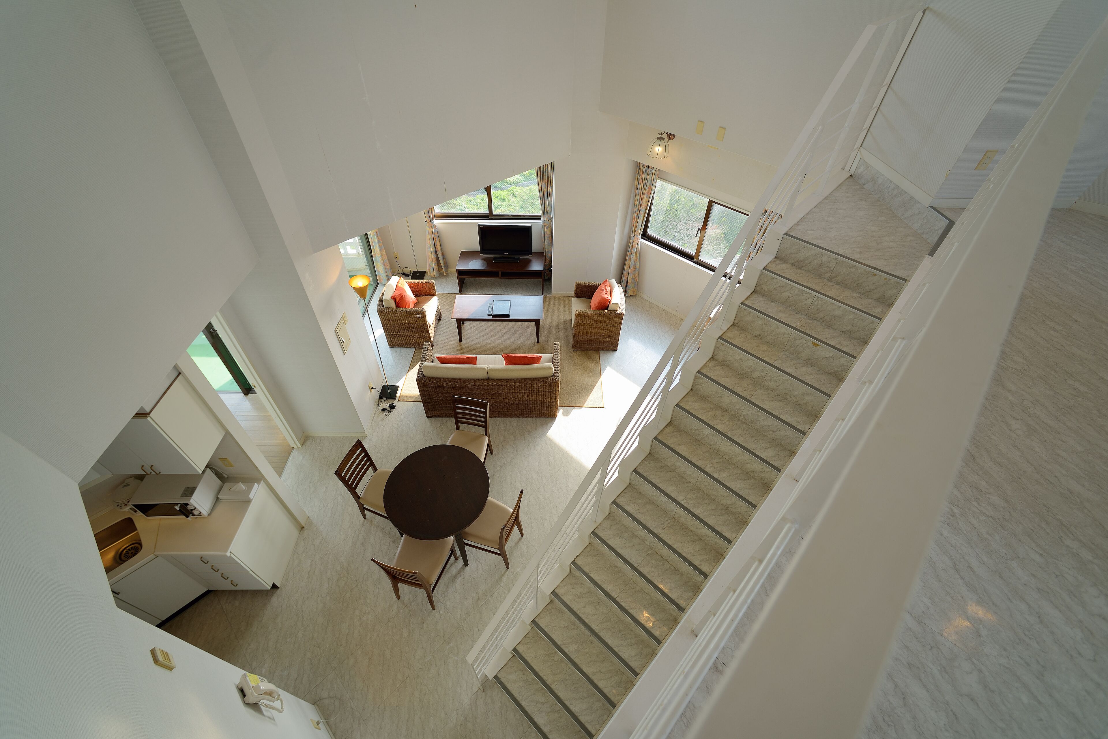 A spacious living area with a sofa set, a coffee table, and a TV. There is a staircase leading to another level.