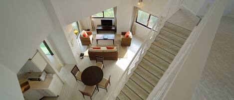 A spacious living area with a sofa set, a coffee table, and a TV. There is a staircase leading to another level.