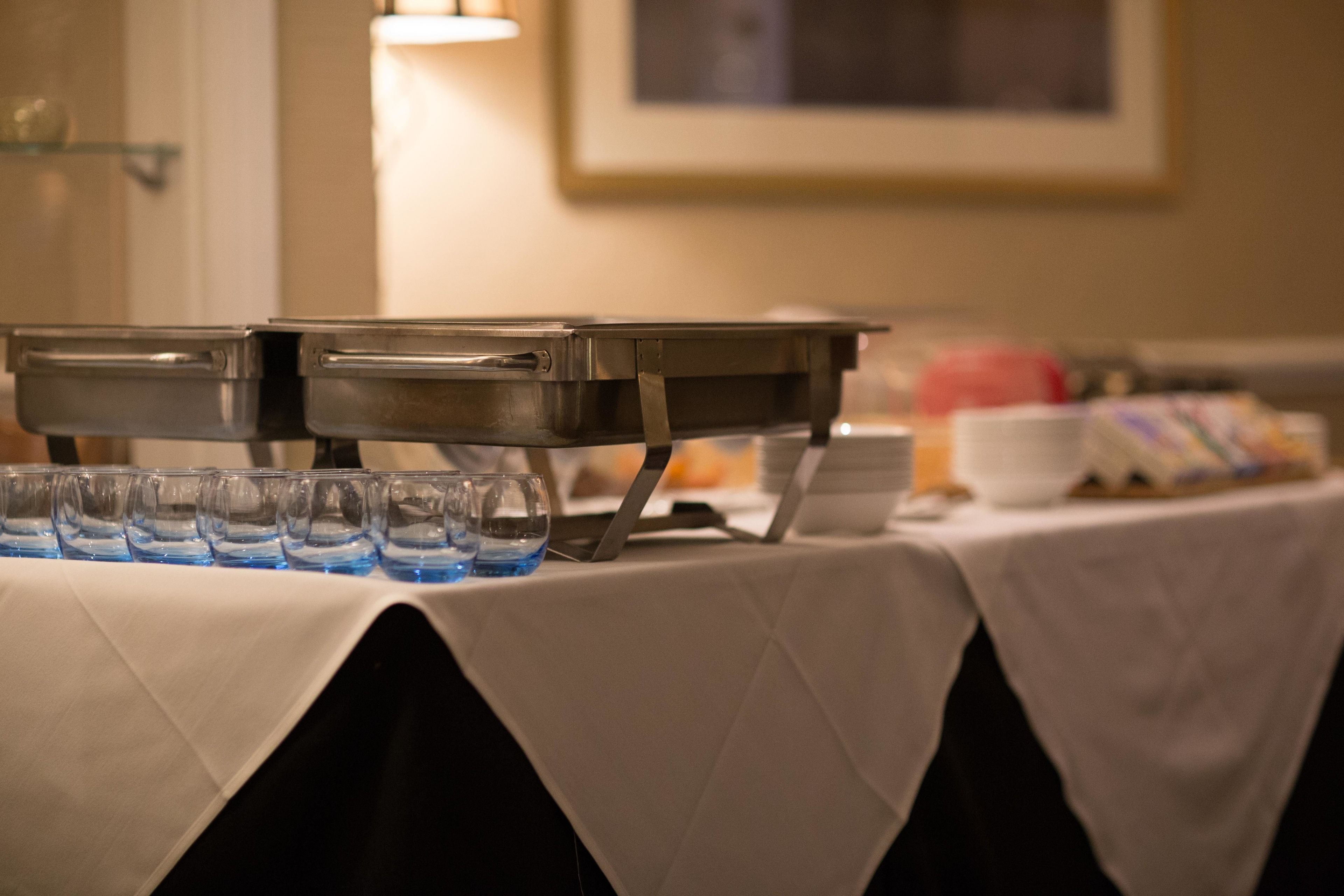 A buffet setup with multiple serving trays and glasses of water.