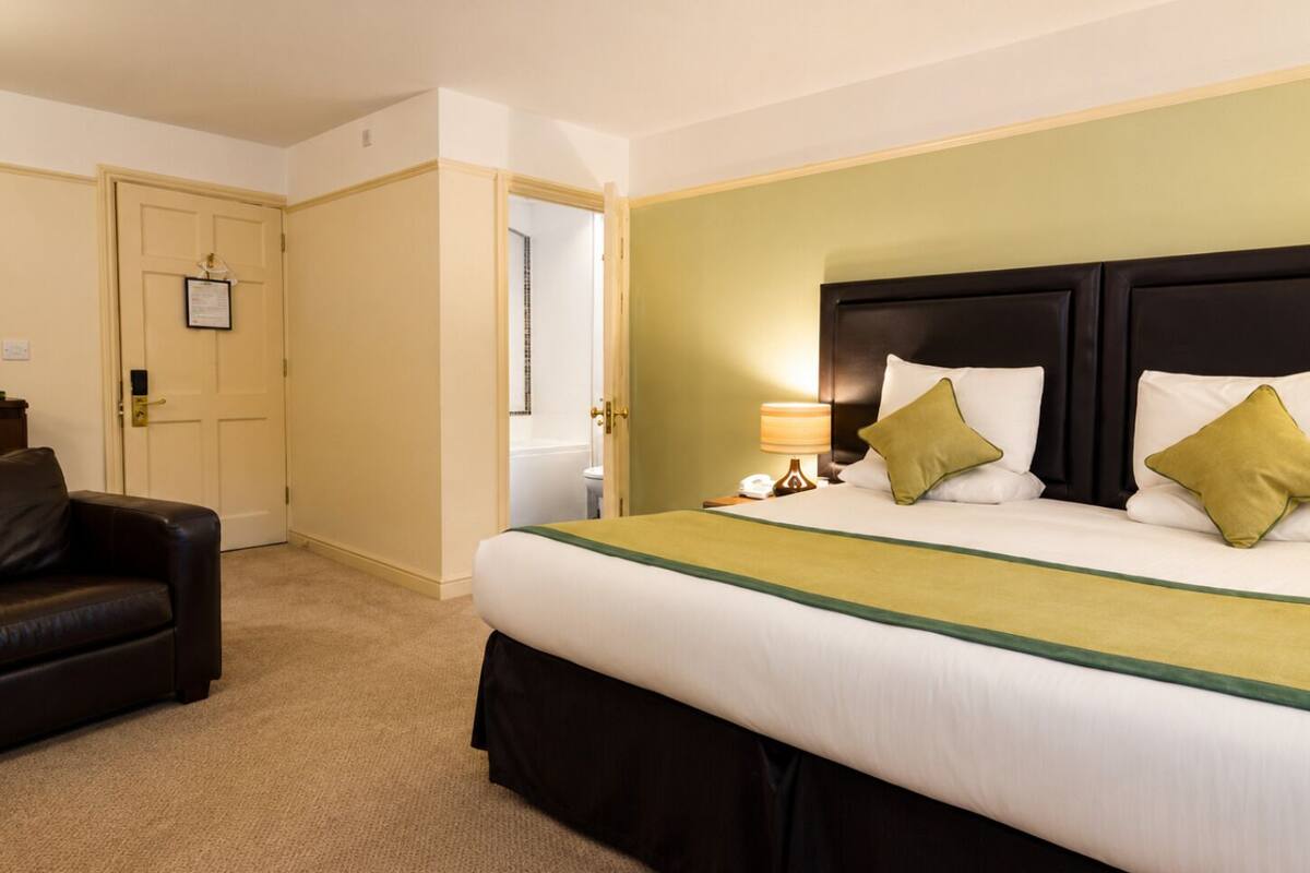 A hotel room with a large bed, a desk, a chair, and a door.