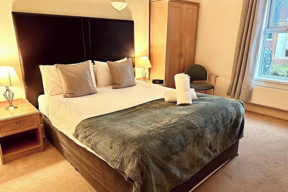A hotel room with a large bed, a nightstand, a wardrobe, and a window with a view.
