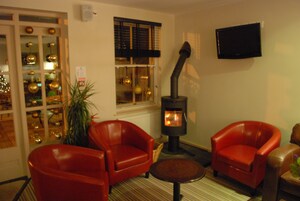 A cozy room with two red leather chairs, a small round table, a wood-burning stove, and a TV mounted on the wall.