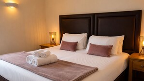 Una cama bien hecha con ropa de cama blanca y marrón, dos mesitas de noche con lámparas y un cabecero.