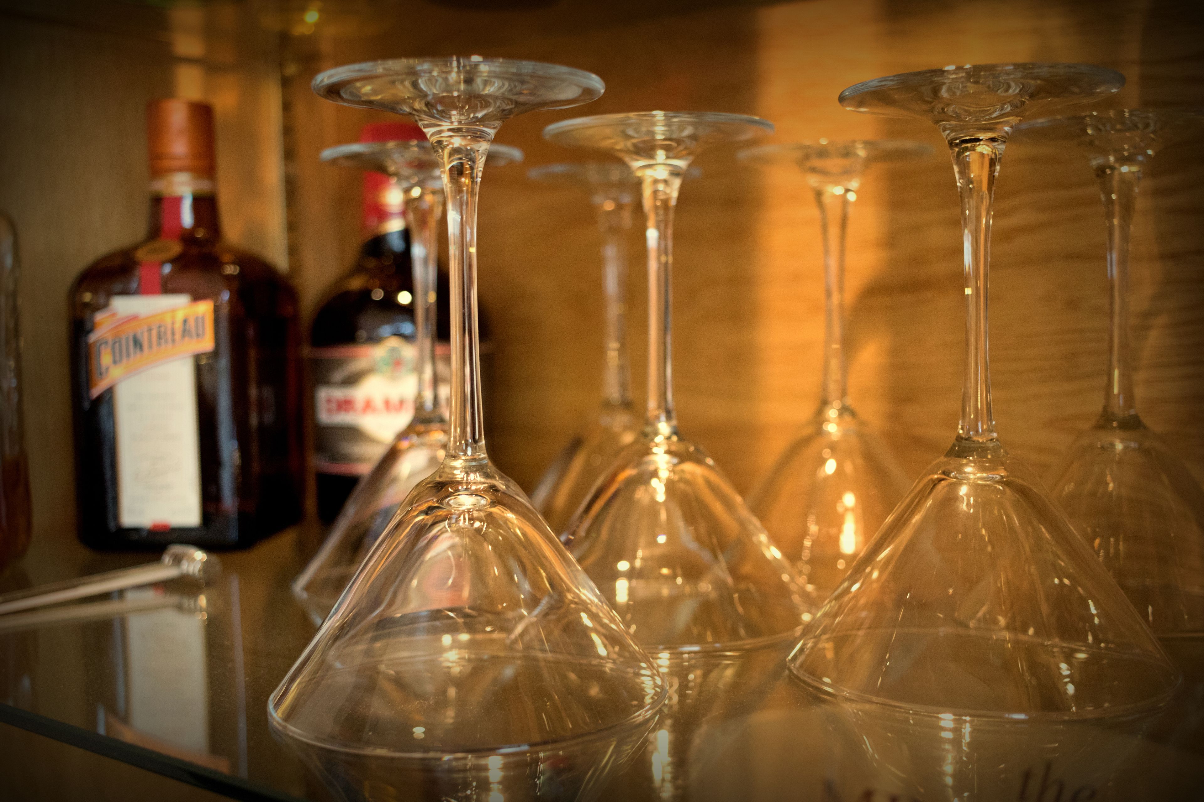 Varias copas de vino sobre una barra, con botellas de licores al fondo.
