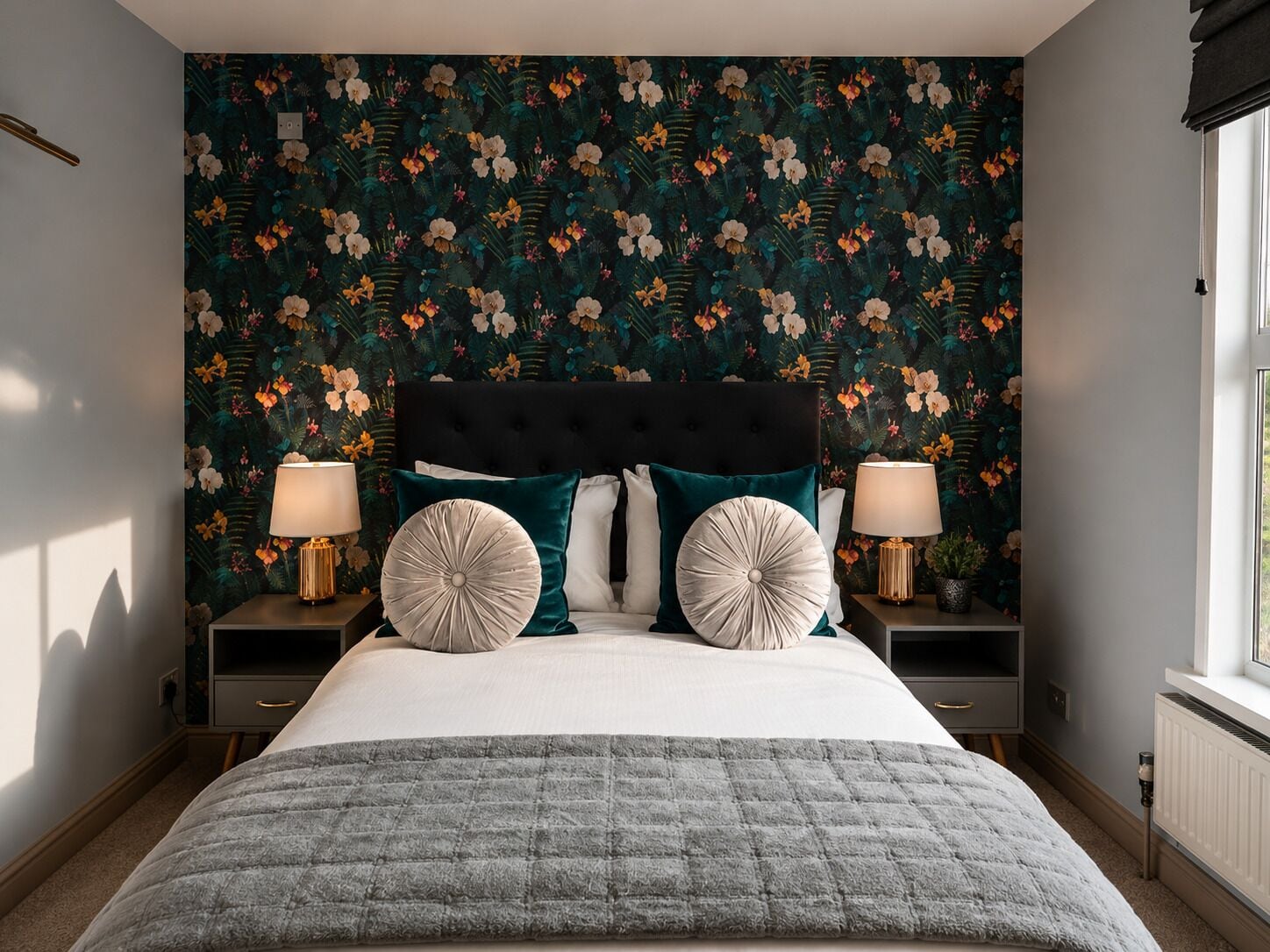 A bedroom with a floral wallpaper, a tufted headboard, two bedside tables with lamps, and a grey quilted bedspread.