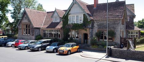 Un bâtiment historique doté d’une façade en pierre, de nombreuses fenêtres et d’un parking où sont garées différentes voitures.