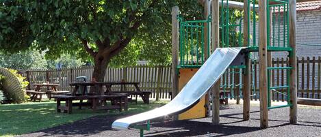 A playground with a slide, picnic tables, and a wooden fence.