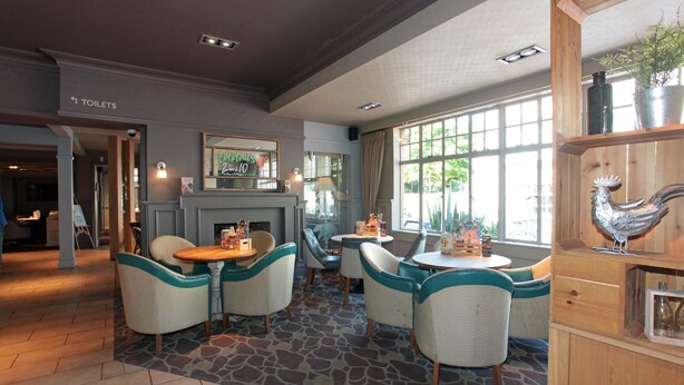 A hotel lobby with a stone floor, teal and white chairs, a fireplace, and a large window with a view of greenery. - Bear Inn, Somerset by Marston's Inns (Street)