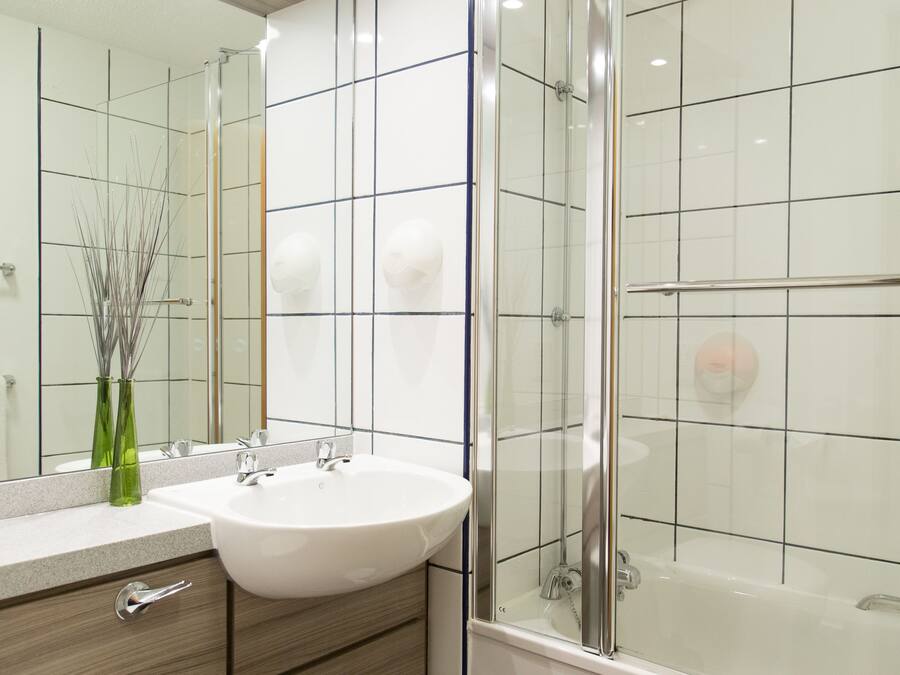 A modern bathroom with a white sink, a glass shower enclosure, and a mirror reflecting the room.