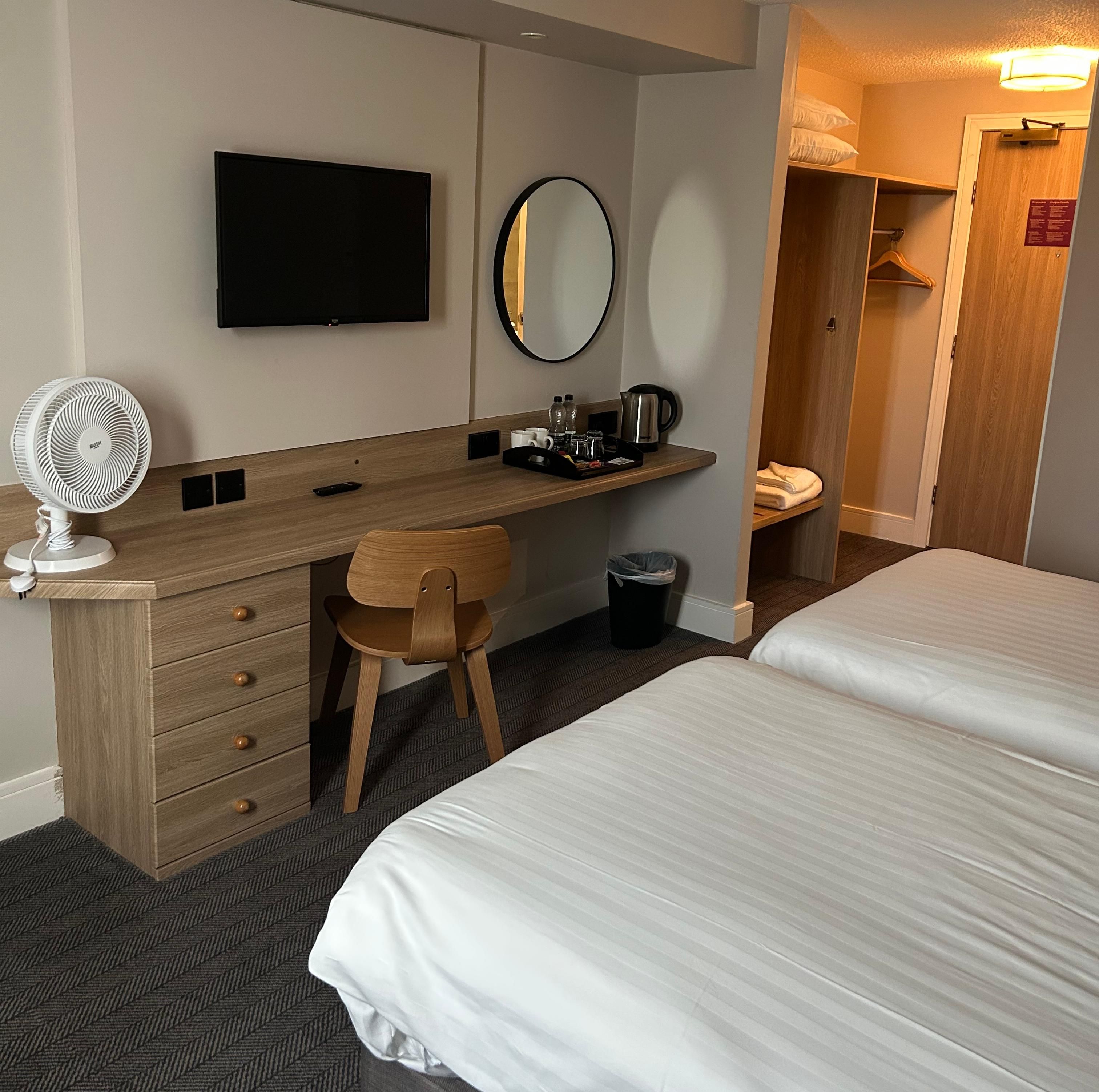 Camera d'albergo con un letto, una scrivania con una sedia, una televisione, uno specchio e un cestino portarifiuti.
