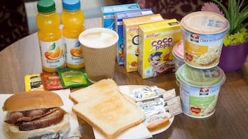 A breakfast table with toast, a sandwich, juice, cereal, and a coffee cup.