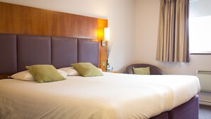 Una cama bien hecha con cabecera de madera, una mesita de noche con lámpara y una ventana con cortinas.
