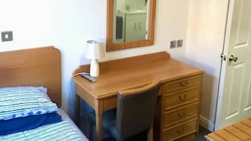 Habitación de hotel con cama, escritorio con silla, cómoda, espejo y puerta.