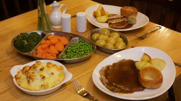 A table with various dishes including a plate with Yorkshire pudding, a plate with gravy and potatoes, a bowl of peas, a bowl of carrots, and a bowl of broccoli.