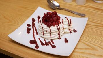 Ein Dessert auf einem weißen Teller mit Himbeertoppings und Sauce auf einer Holztischplatte.