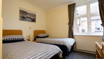 A room with two beds, a window with curtains, a radiator, and a painting on the wall.