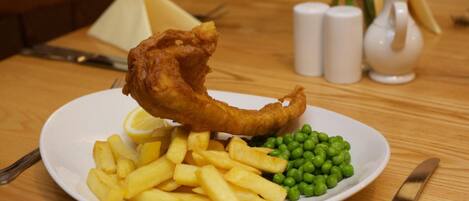 A plate of fish and chips with peas and lemon on a wooden table.